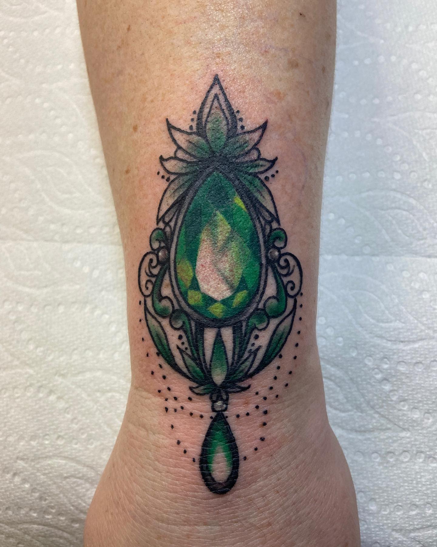 Intricate green gemstone tattoo with ornate black detailing on an arm